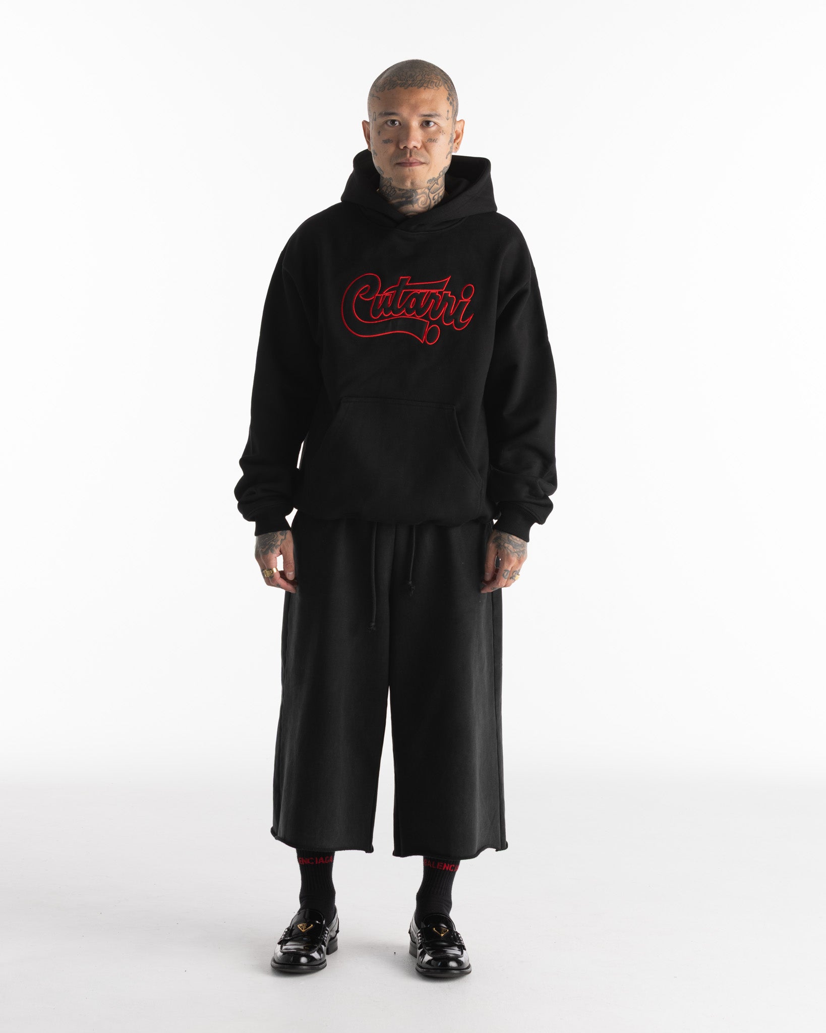 Person wearing a black hoodie with red text and black pants on a white background