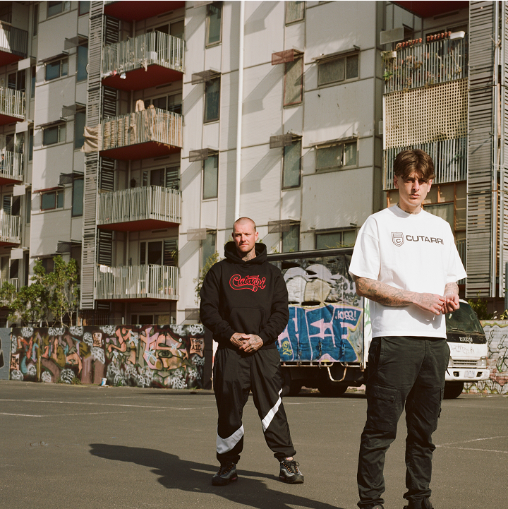 Two men standing on a street with an apartment building in the background