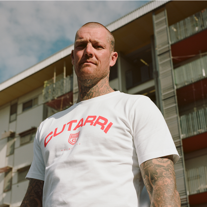 Man wearing a white t-shirt with red text standing in front of a building